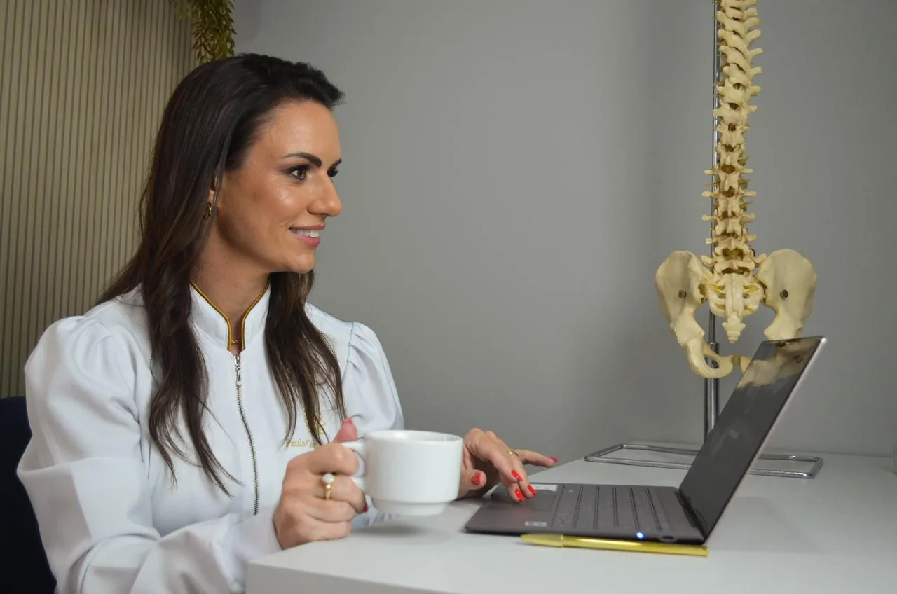Paula trabalhando no computador ao lado de um modelo da coluna